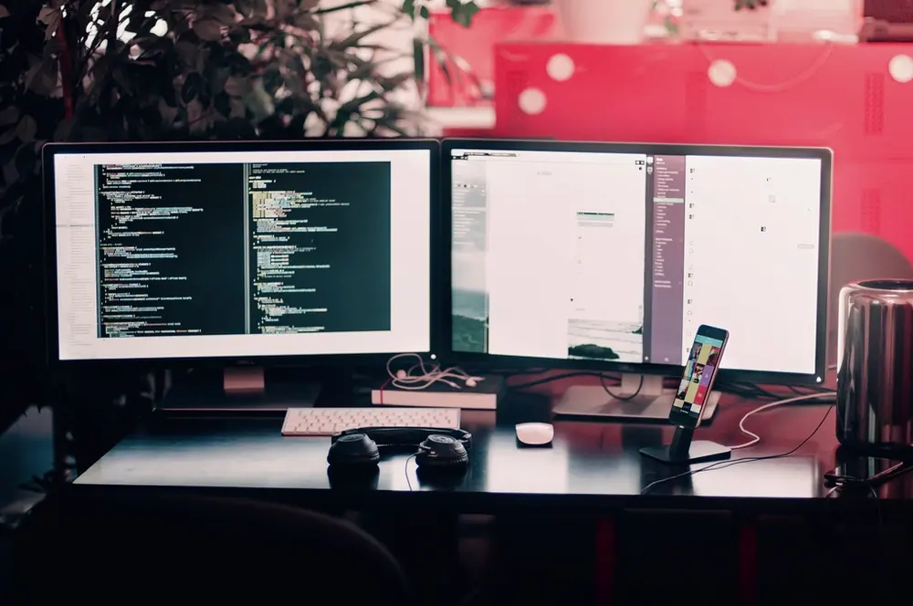 Dual-monitor development workspace with code and a mobile device